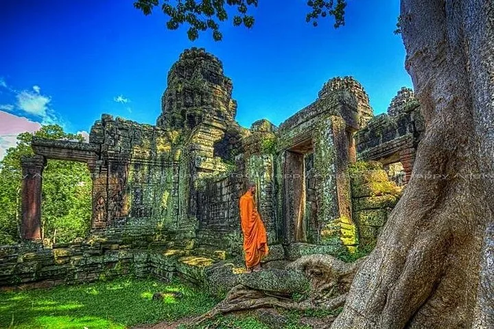 Monje con túnicas naranjas de pie entre antiguas ruinas de templos de piedra